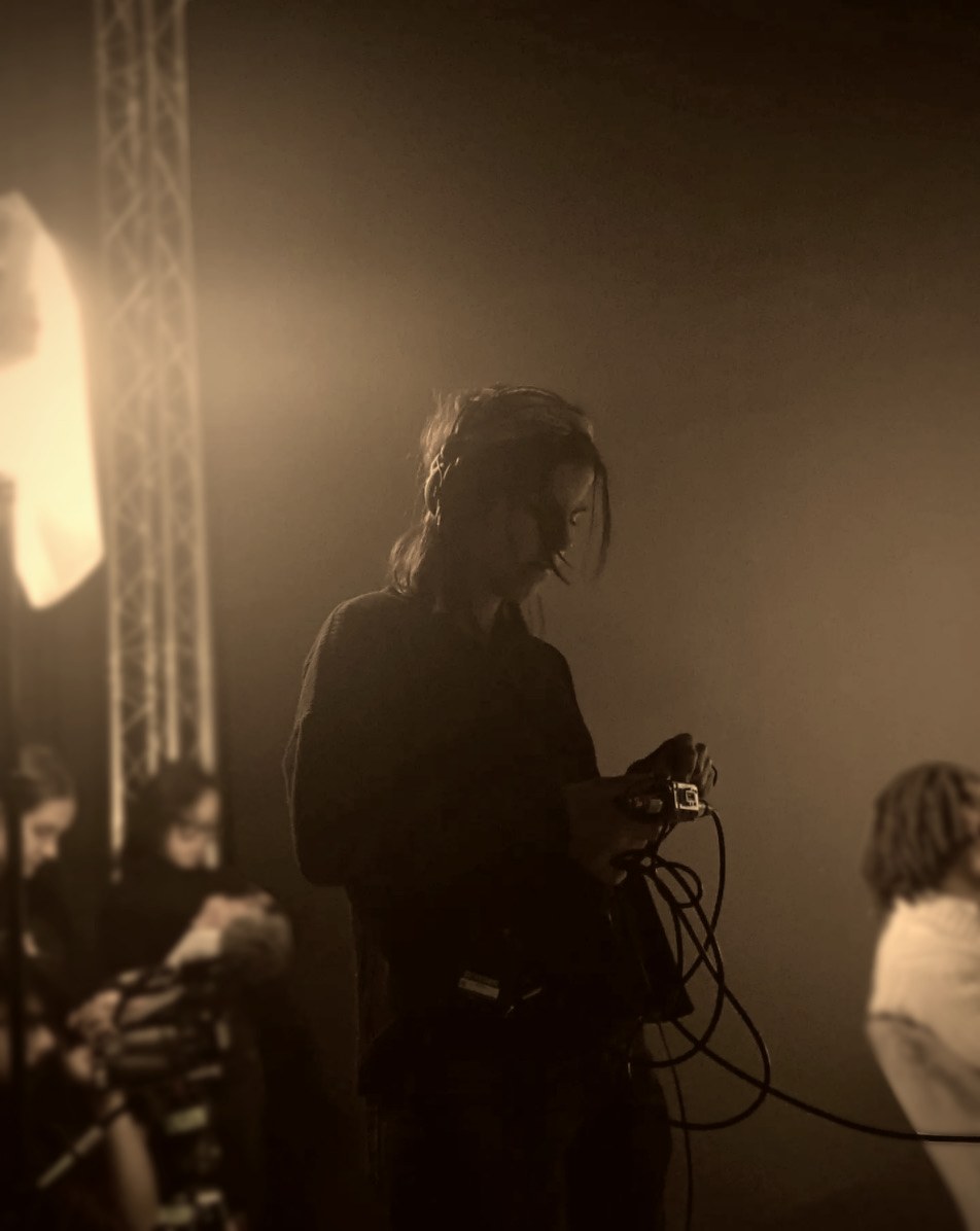 Chloé Latrech on set, backlit by a key light, holding the camera rig.